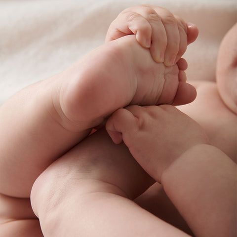 Baby wearing no clothes holding onto its foot