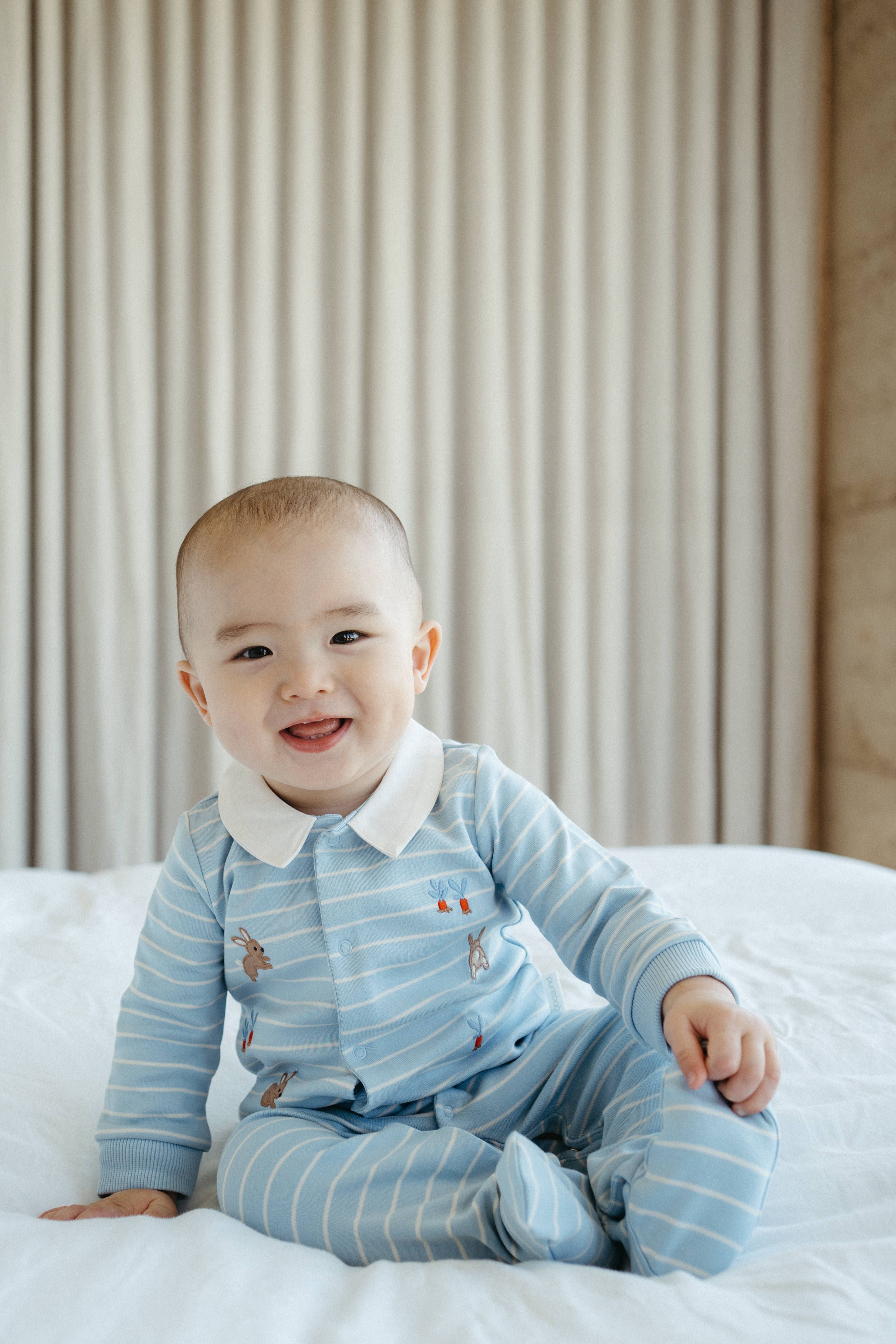 Baby sitting up on bed wearing Easter growsuit
