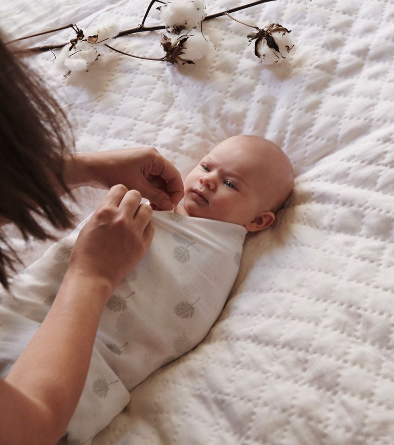 Parent gently swaddling their newborn in a muslin wrap
