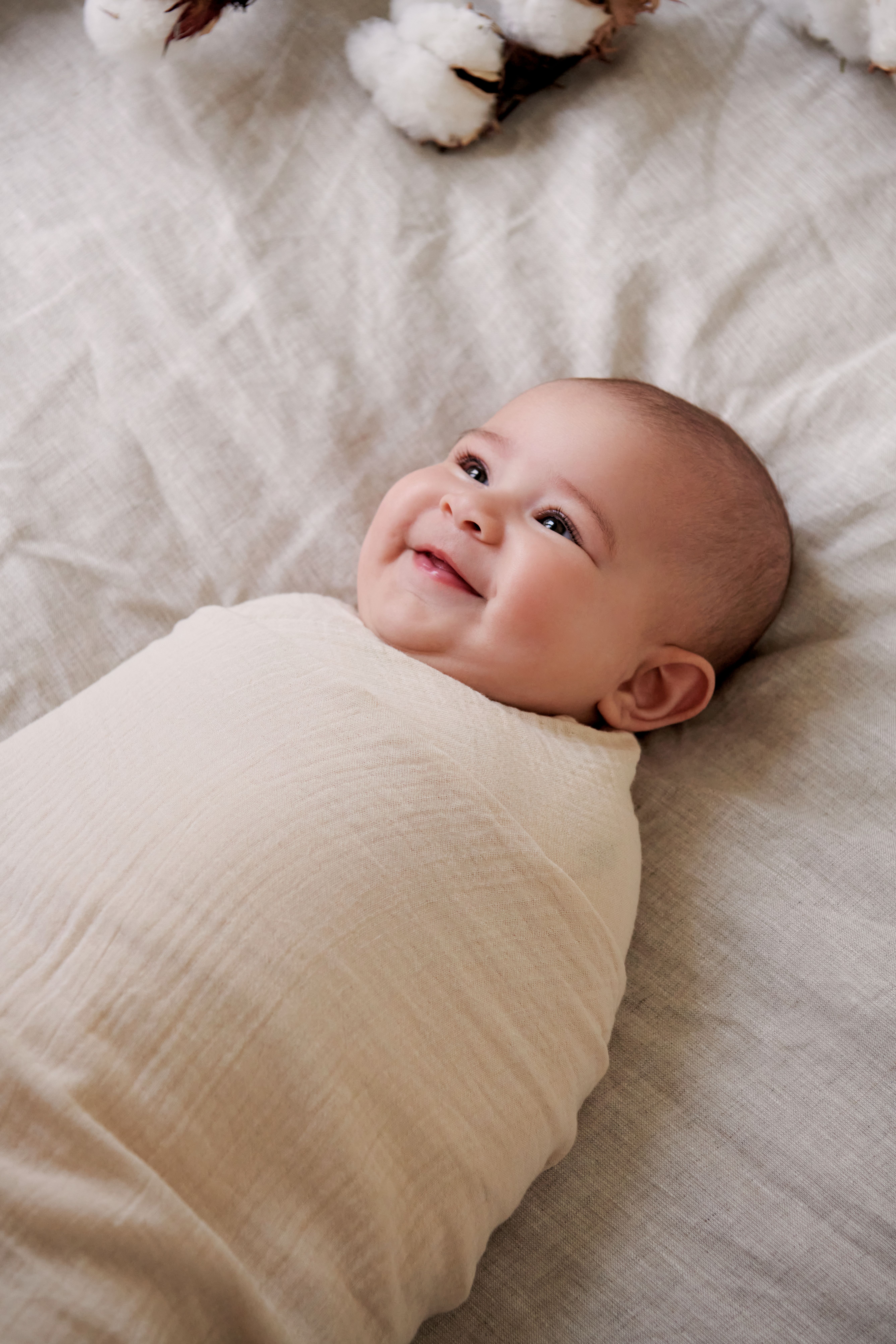 Baby swaddled in muslin wrap laying on bed
