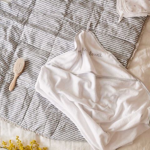 Purebaby hooded towel and baby hair brush laid out on striped blanket