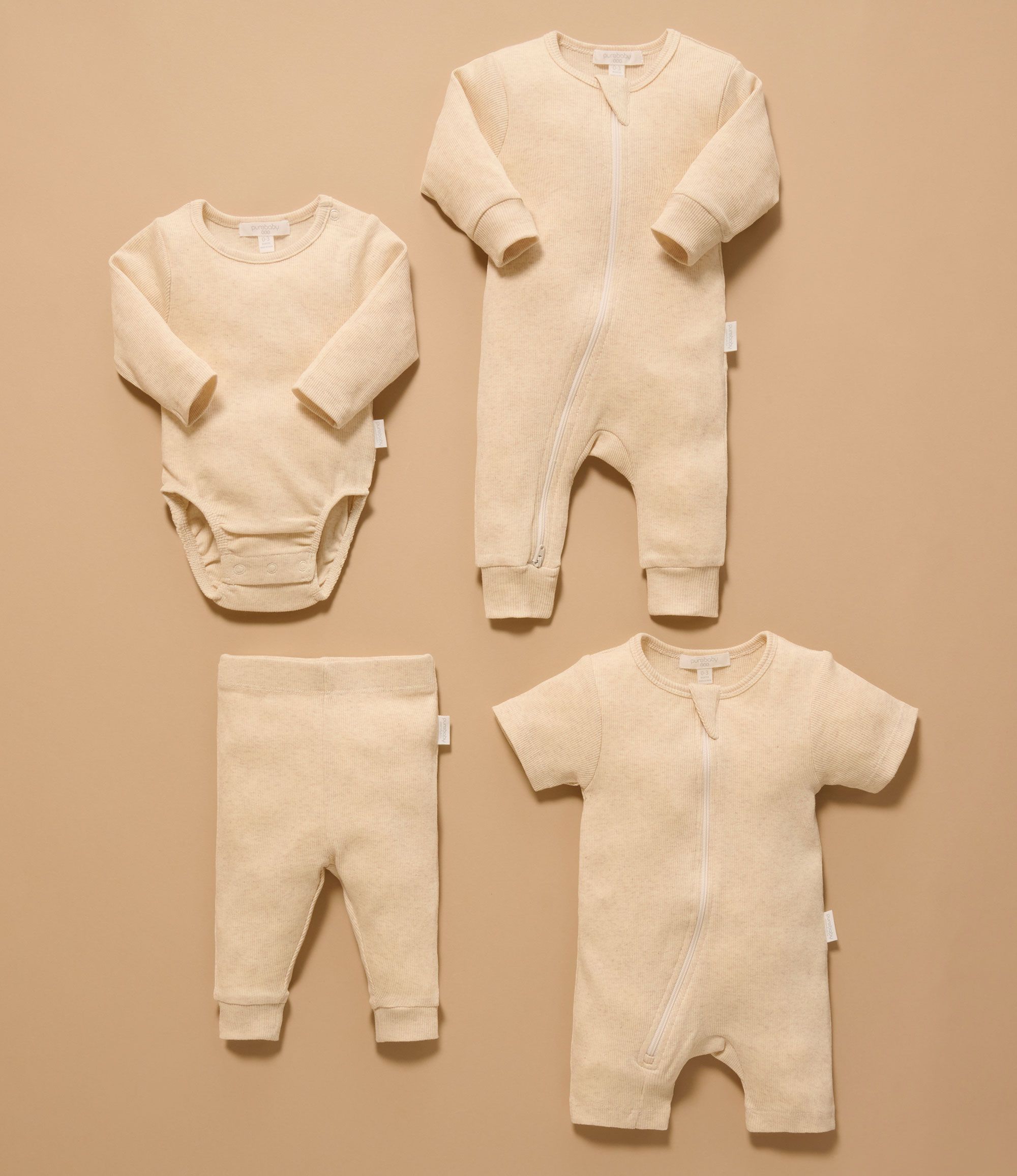 A selection of Purebaby Essentials laid out, including growsuits, bodysuits, and leggings