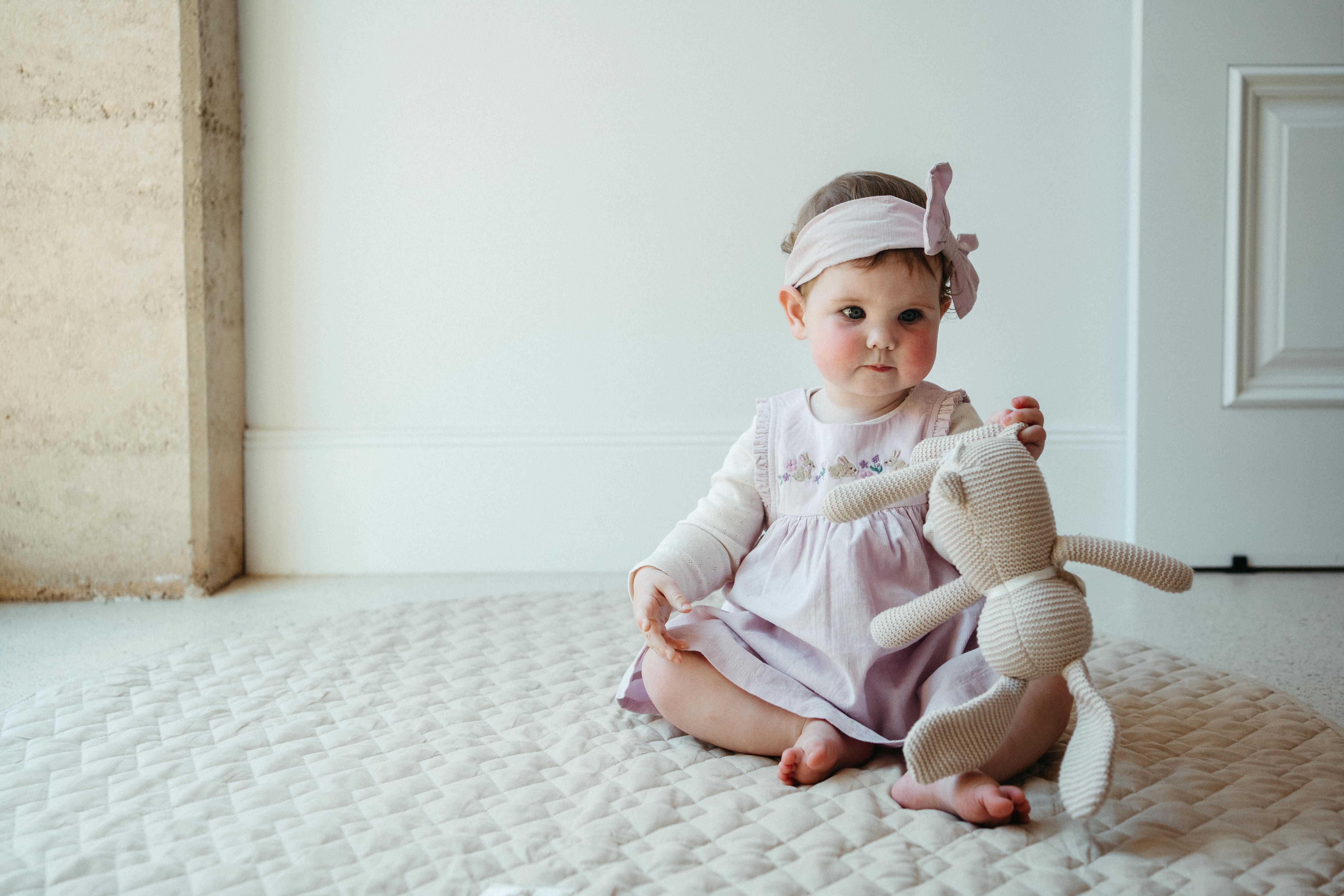 Baby sitting on rug, standing up wearing Easter outfit